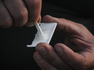 Worker prepairing glue on a small white plastic piece. Man's hands, close up. Glue mixing.