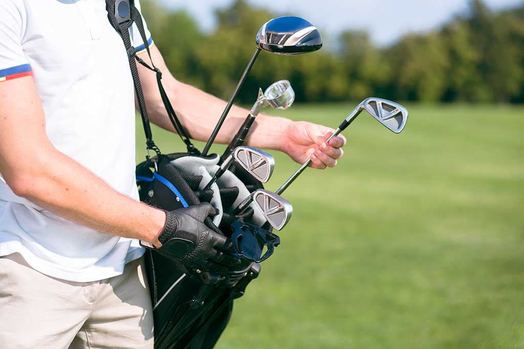 Man in white tshirt removing a golf club from his golf bag to start playing